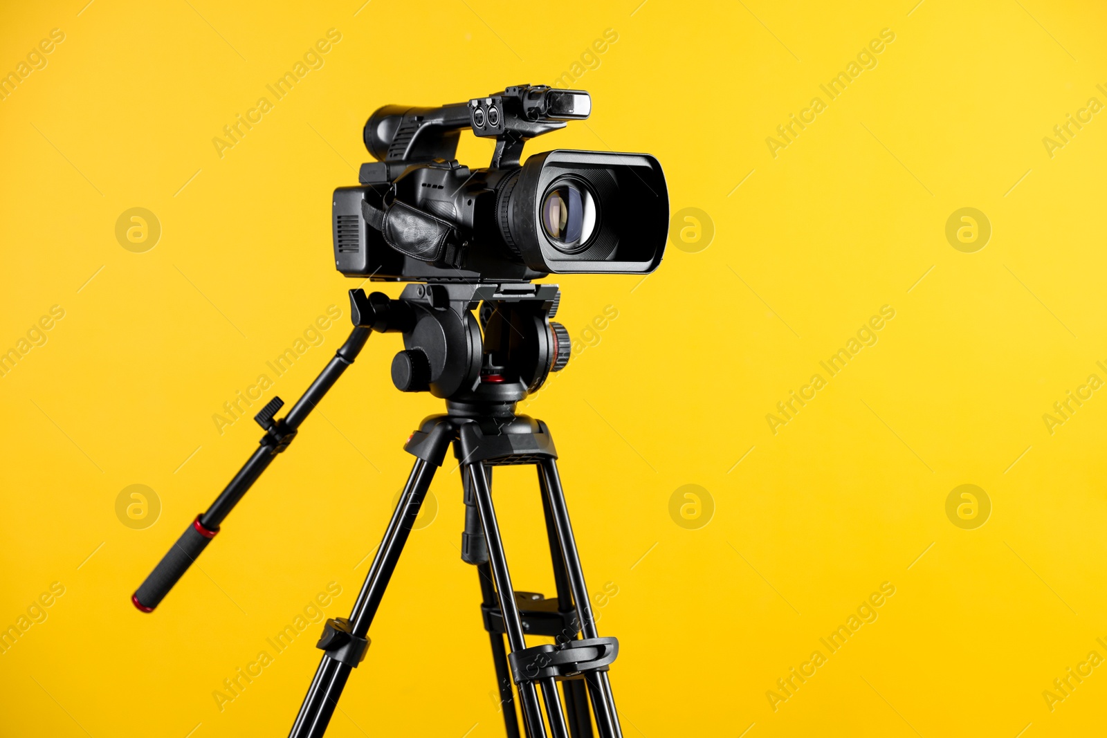 Photo of Modern video camera with tripod on yellow background, space for text