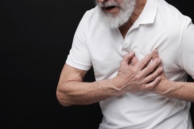 Photo of Heart attack. Senior man suffering from pain in chest on black background, closeup. Space for text