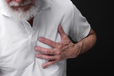 Photo of Heart attack. Senior man suffering from pain in chest on black background, closeup