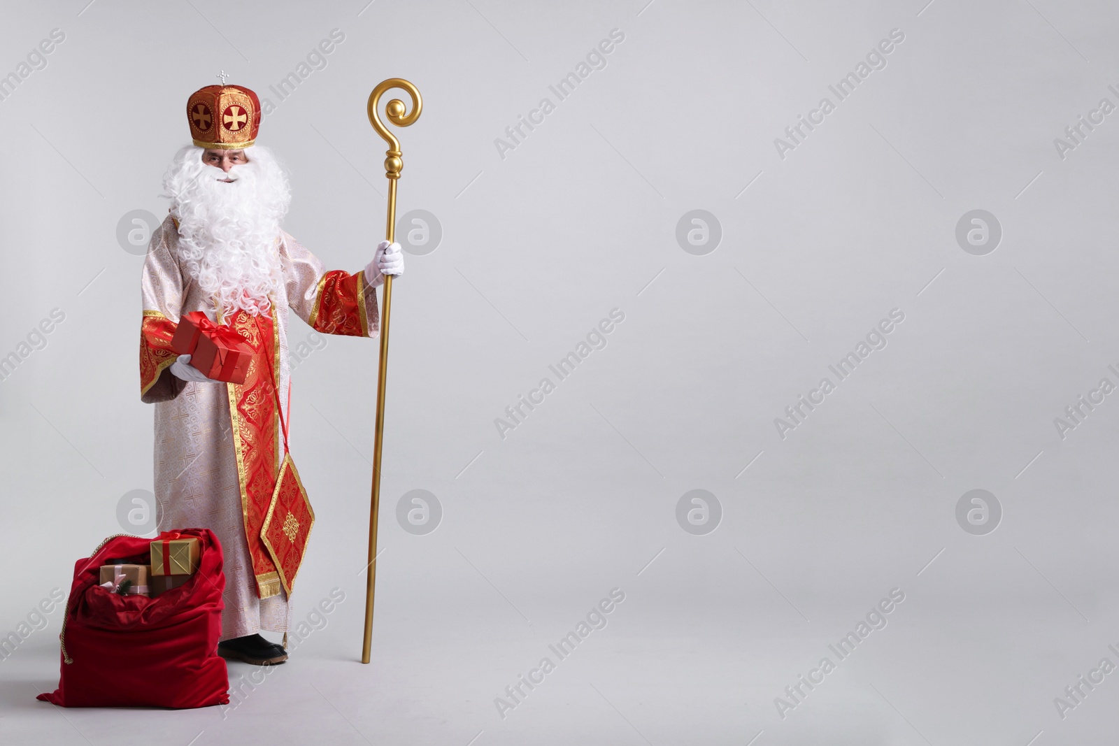 Photo of Saint Nicholas with sack full of gifts on light grey background. Space for text