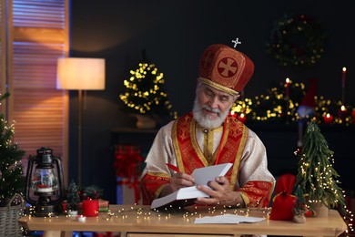 Photo of Saint Nicholas with notebook at desk in room decorated for Christmas