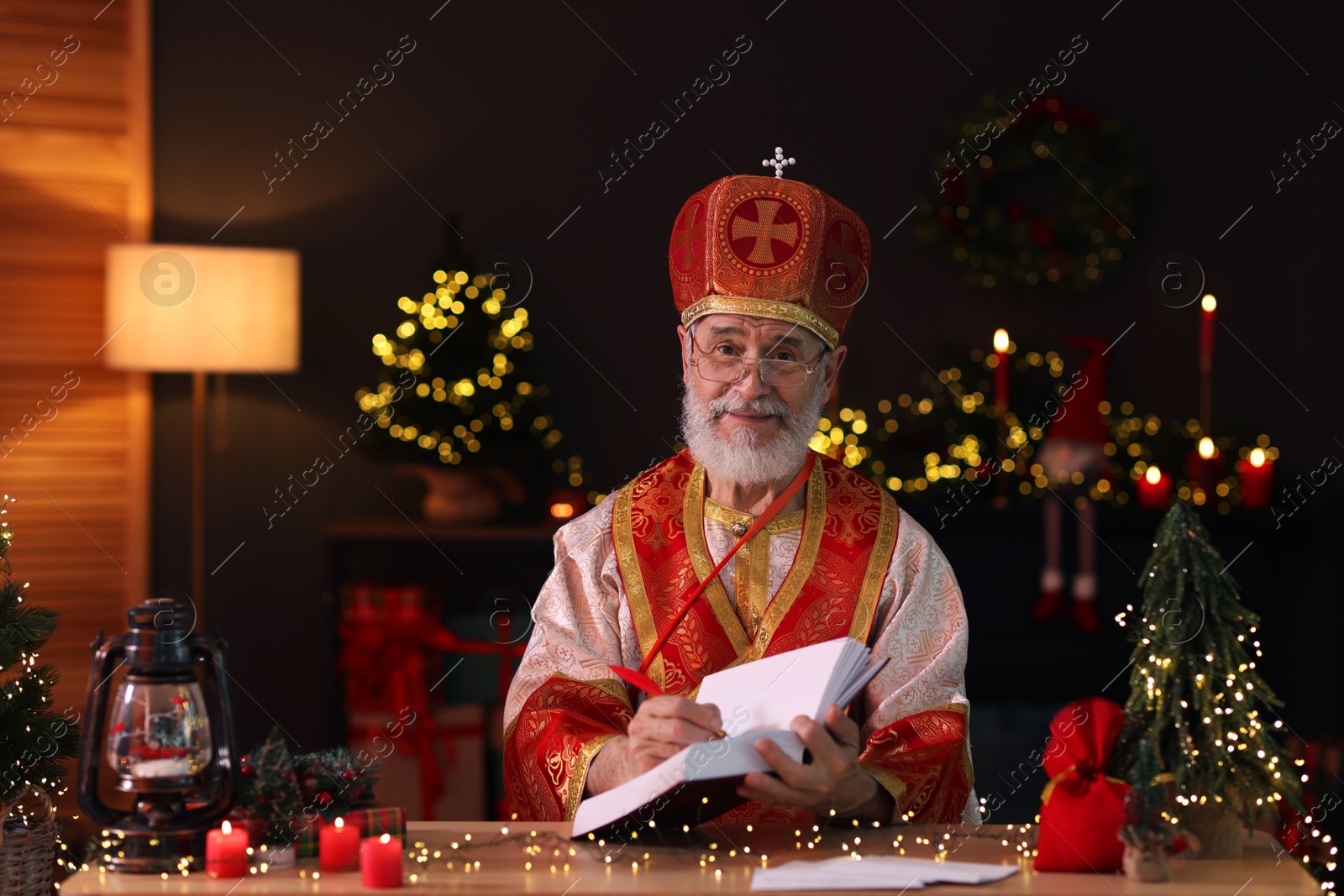 Photo of Saint Nicholas with notebook at desk in room decorated for Christmas