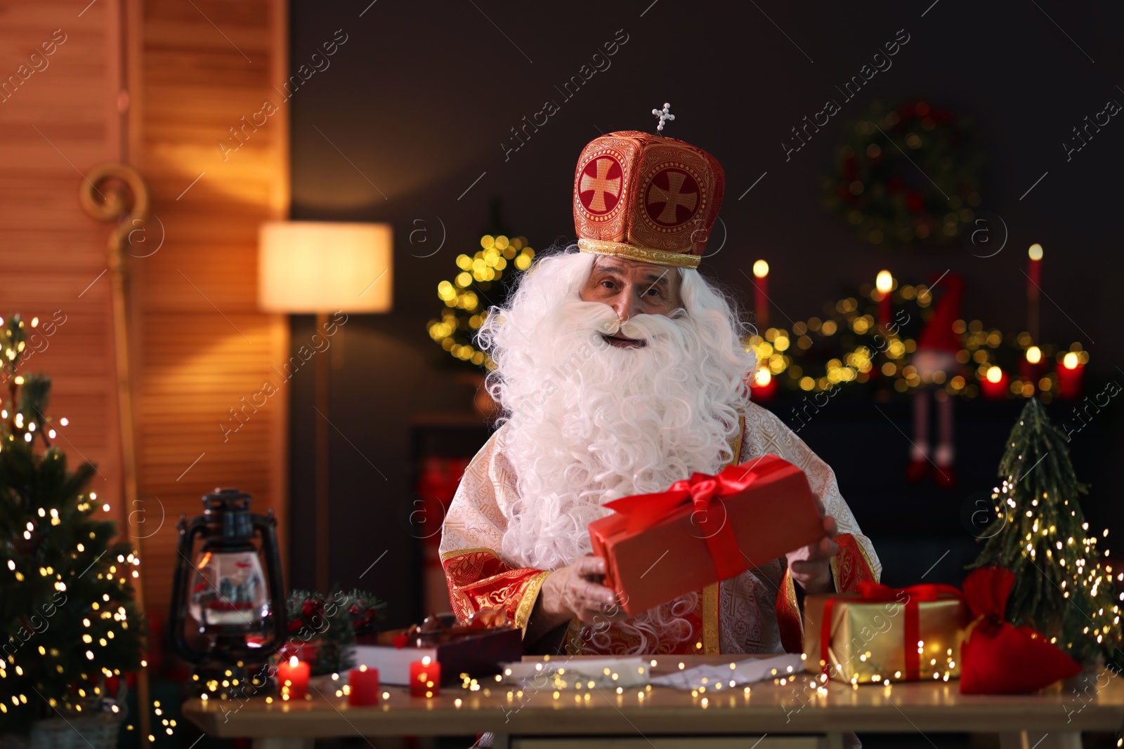 Photo of Saint Nicholas with gifts at desk in room decorated for Christmas