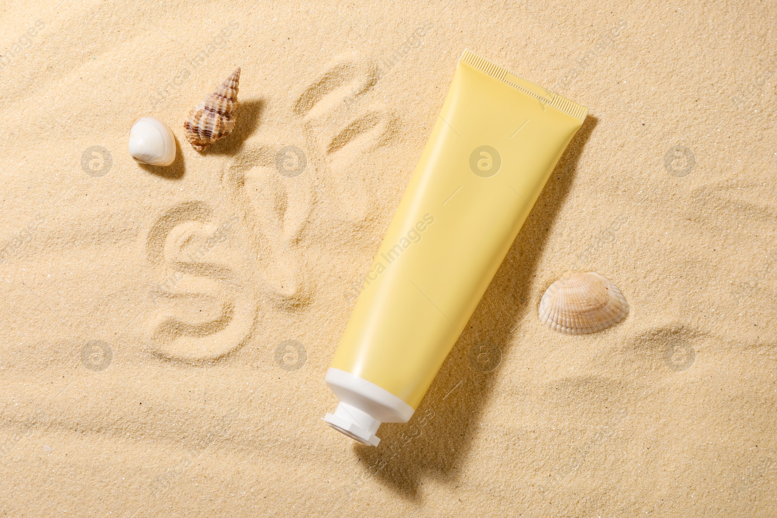 Photo of Abbreviation SPF written on sand, tube of sun protection product and seashells at beach, top view