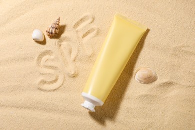 Abbreviation SPF written on sand, tube of sun protection product and seashells at beach, top view