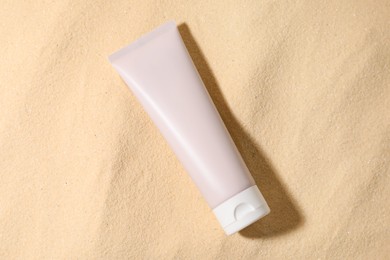 Tube of sun protection product on sand, top view