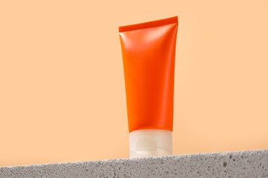 Photo of Tube of sun protection product on stone against beige background, low angle view