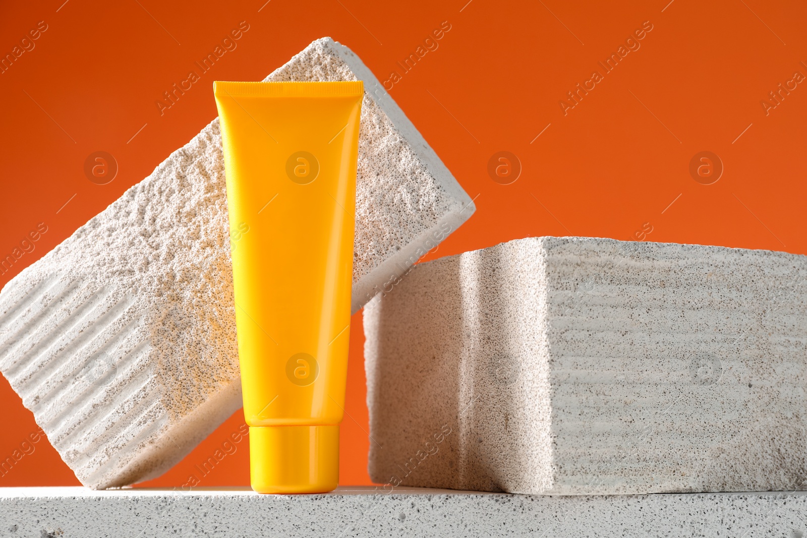 Photo of Tube of sun protection product and stones on orange background