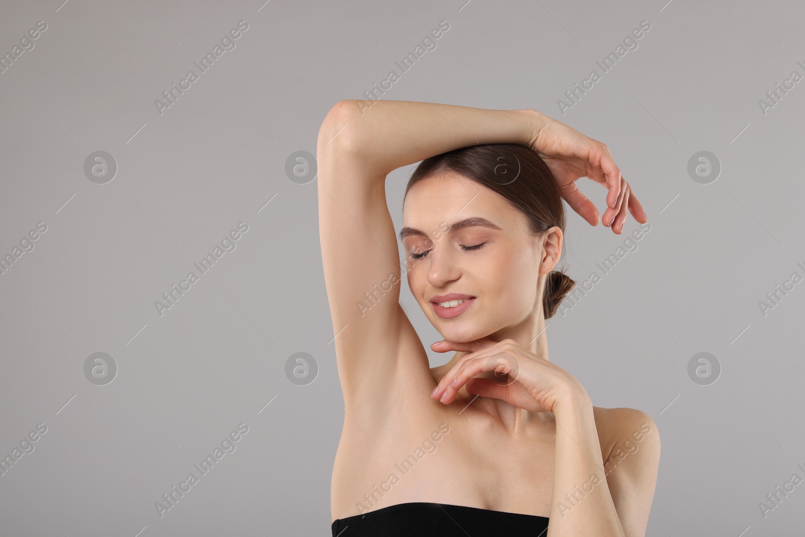 Photo of Young woman showing smooth skin after epilation on gray background