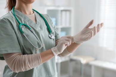 Photo of Medical worker putting on gloves in hospital, closeup