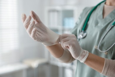 Photo of Medical worker putting on gloves in hospital, closeup