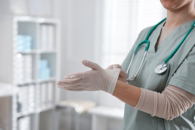 Photo of Medical worker putting on gloves in hospital, closeup. Space for text