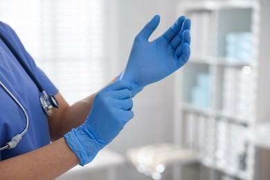 Photo of Medical worker putting on gloves in hospital, closeup