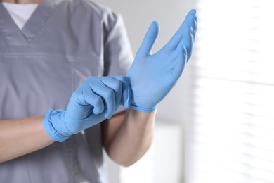 Photo of Medical worker putting on gloves in hospital, closeup