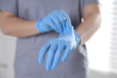 Photo of Medical worker putting on gloves in hospital, closeup