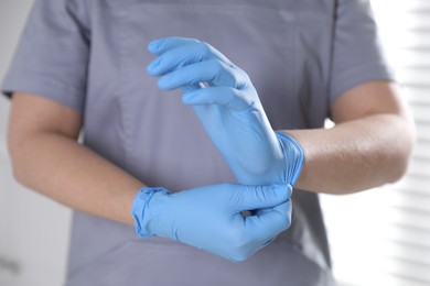 Photo of Medical worker putting on gloves in hospital, closeup