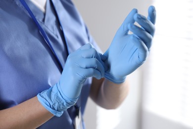 Photo of Medical worker putting on gloves in hospital, closeup