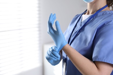 Photo of Medical worker putting on gloves in hospital, closeup. Space for text