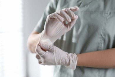 Photo of Medical worker putting on gloves in hospital, closeup