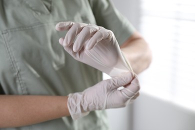 Photo of Medical worker putting on gloves in hospital, closeup