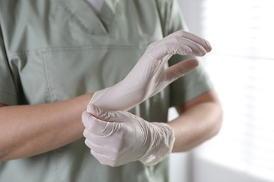 Photo of Medical worker putting on gloves in hospital, closeup