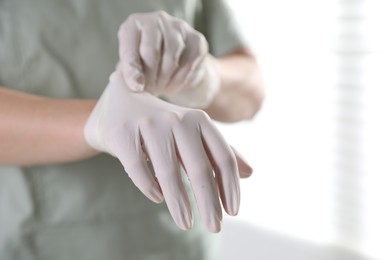 Photo of Medical worker putting on gloves in hospital, closeup