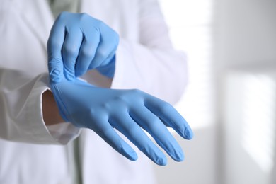 Photo of Medical worker putting on gloves in hospital, closeup