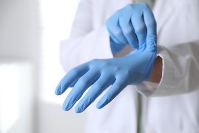 Photo of Medical worker putting on gloves in hospital, closeup