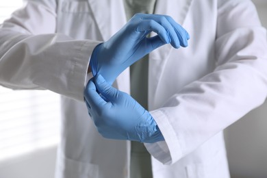 Photo of Medical worker putting on gloves in hospital, closeup