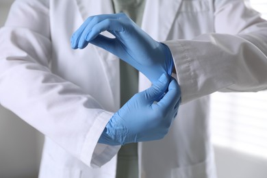 Photo of Medical worker putting on gloves in hospital, closeup