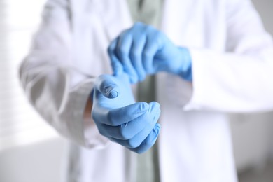 Photo of Medical worker putting on gloves in hospital, closeup