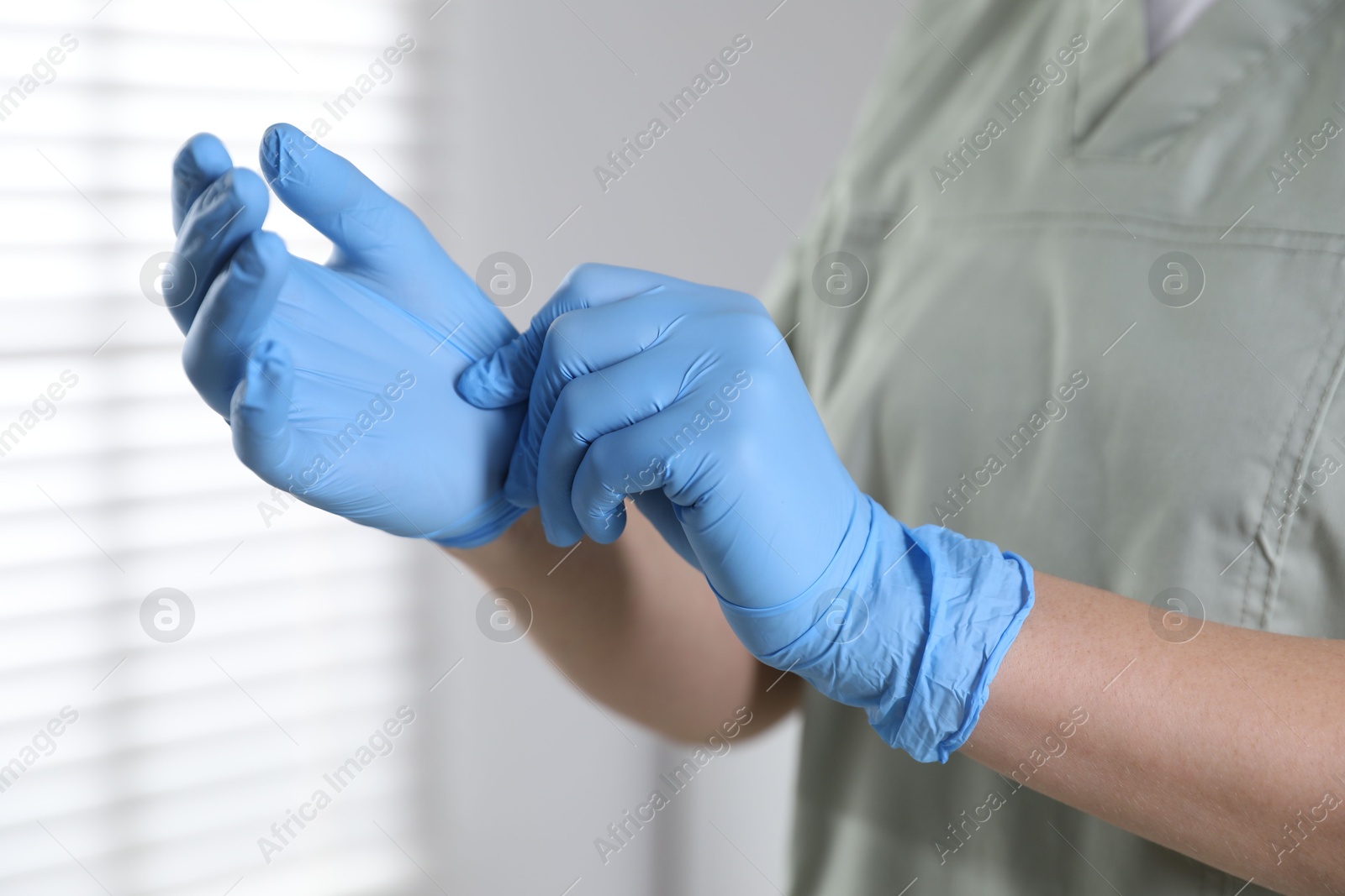 Photo of Medical worker putting on gloves in hospital, closeup