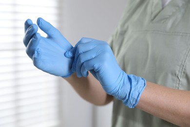 Photo of Medical worker putting on gloves in hospital, closeup