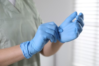 Photo of Medical worker putting on gloves in hospital, closeup