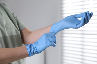 Photo of Medical worker putting on gloves in hospital, closeup