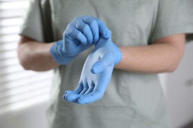 Photo of Medical worker putting on gloves in hospital, closeup