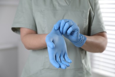 Photo of Medical worker putting on gloves in hospital, closeup