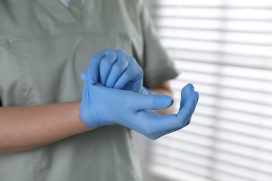 Photo of Medical worker putting on gloves in hospital, closeup