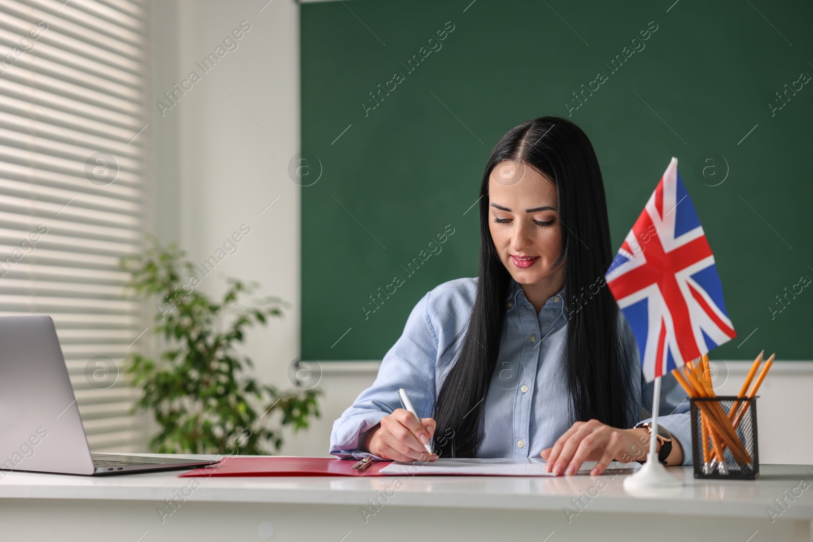 Photo of English teacher working at desk in classroom. Space for text