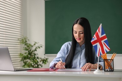 Photo of English teacher working at desk in classroom. Space for text