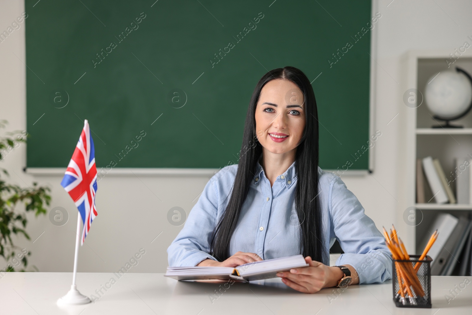 Photo of English teacher with book at desk in classroom