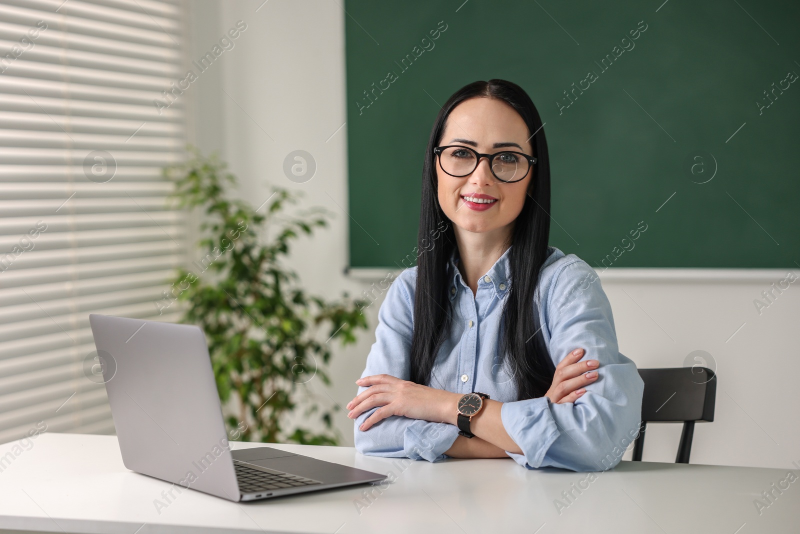 Photo of English teacher with laptop at desk in classroom. Space for text