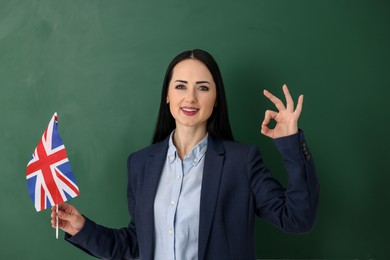 English teacher with UK flag showing ok gesture near chalkboard in classroom