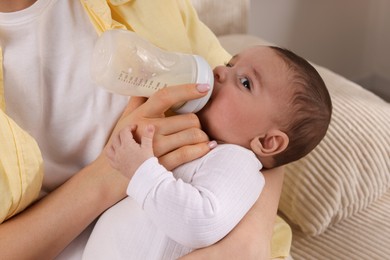 Photo of Mother feeding her little baby from bottle indoors, closeup