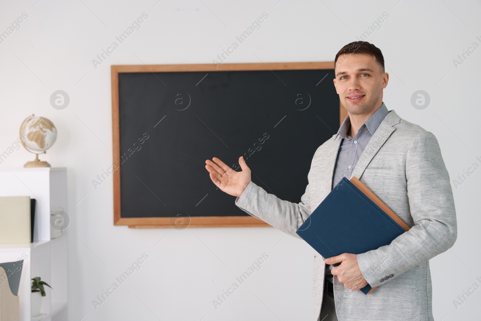 Photo of English teacher with books against blackboard in classroom