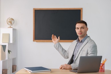 Photo of English teacher working at desk in classroom. Space for text