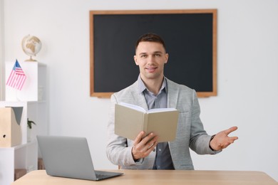 English teacher with book working at desk in classroom