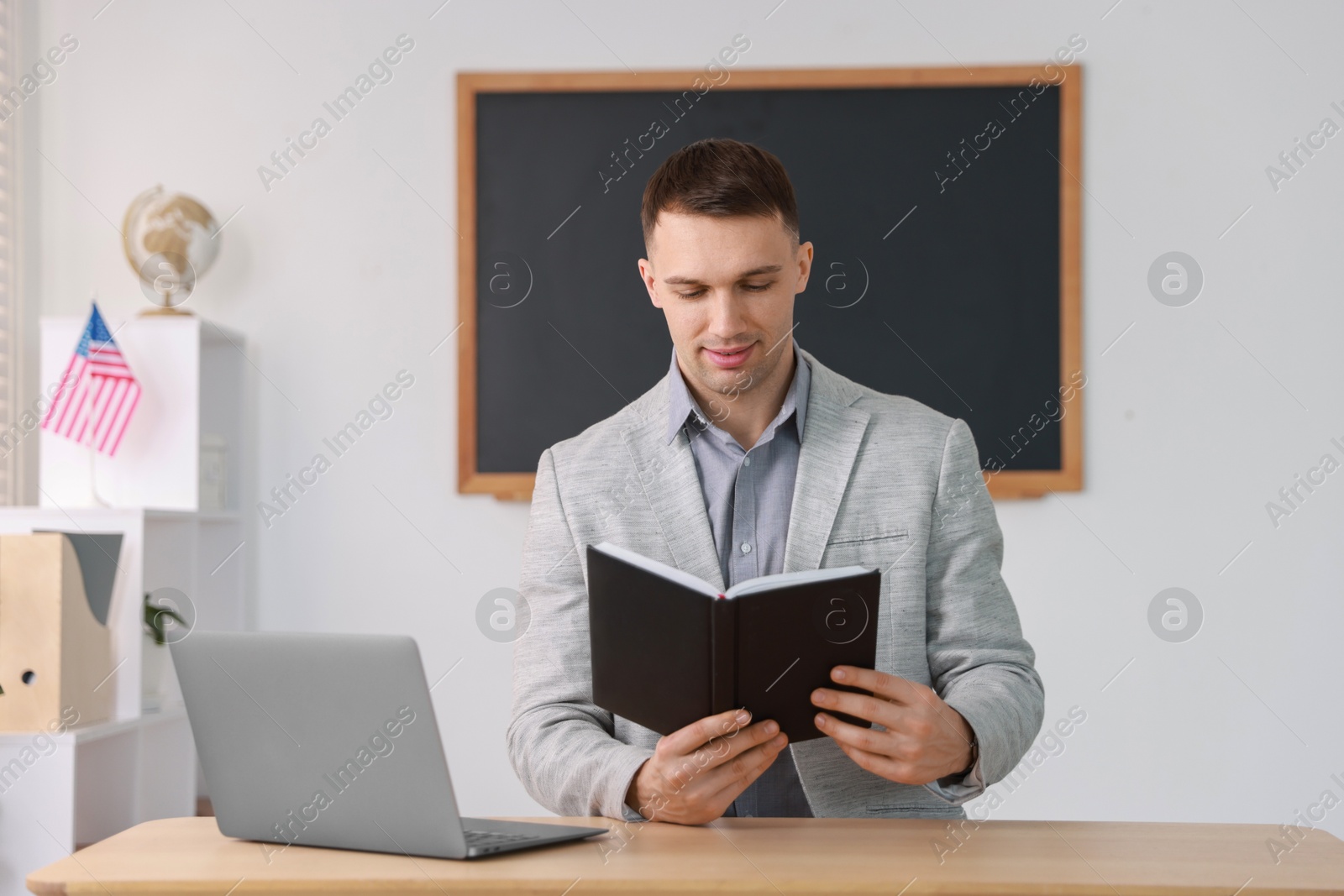 Photo of English teacher with book working at desk in classroom