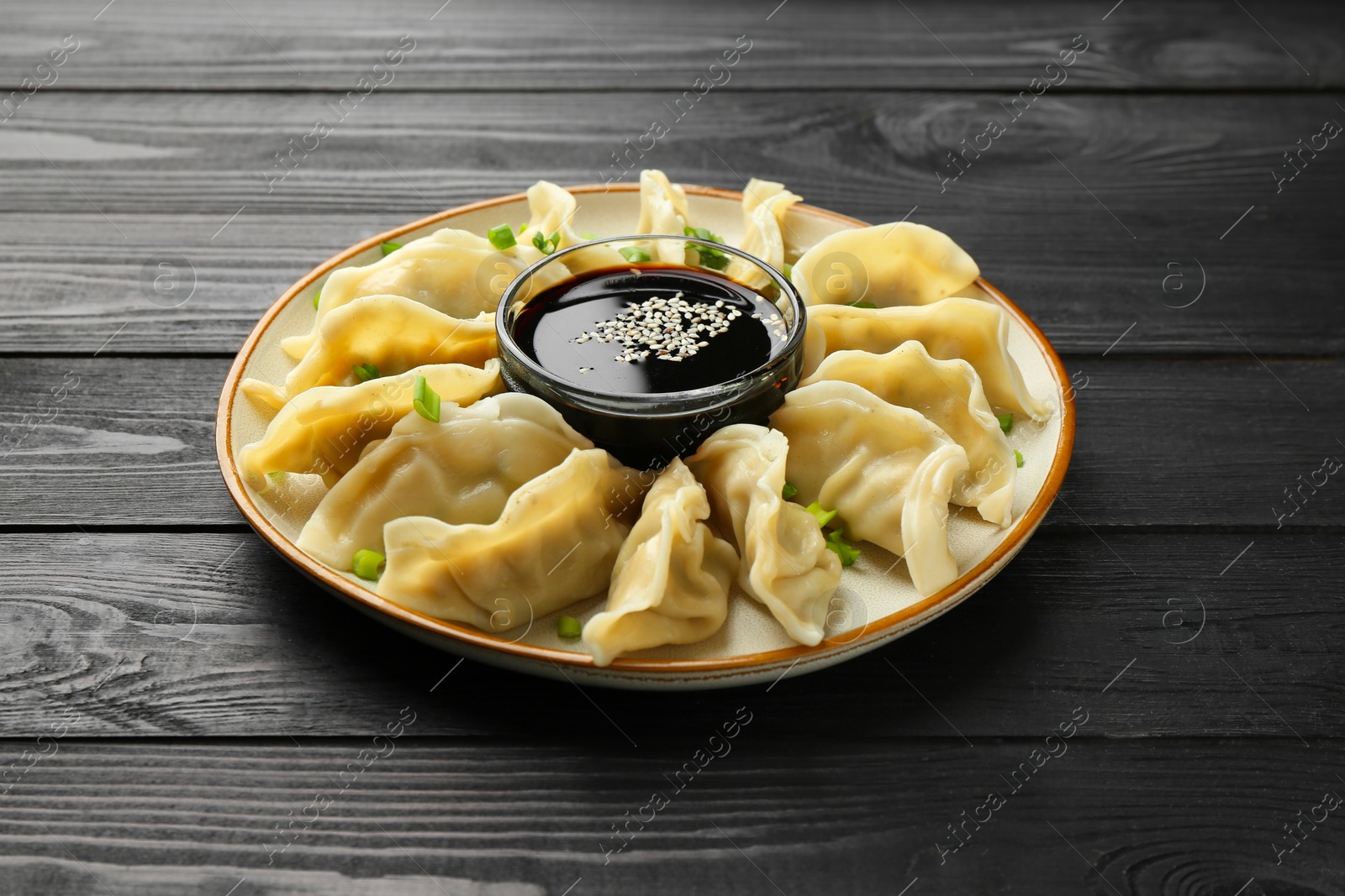 Photo of Tasty boiled gyoza (dumplings) with green onion and soy sauce on black wooden table