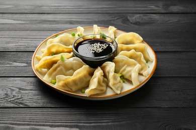 Tasty boiled gyoza (dumplings) with green onion and soy sauce on black wooden table